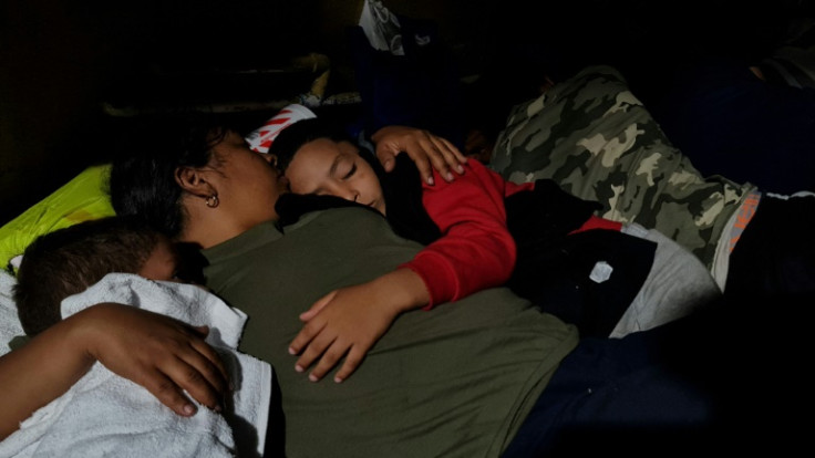 Dasling Sanchez sostiene a sus hijos dormidos mientras descansan junto a una gasolinera en el centro de Brownsville, Texas, el 6 de mayo de 2023.