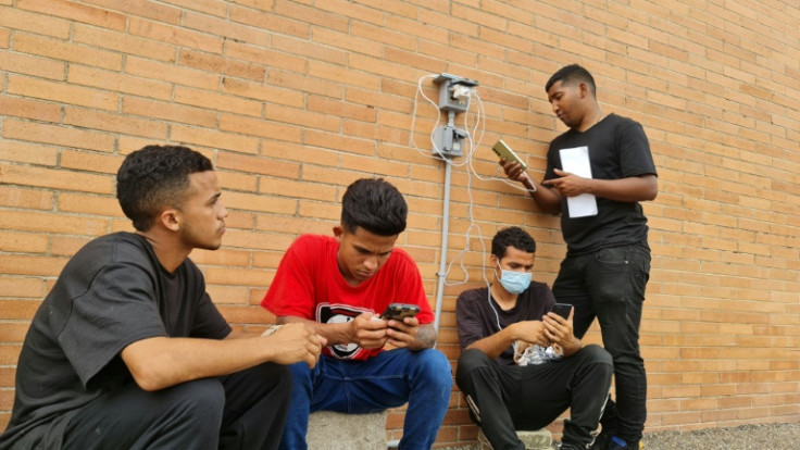Un grupo de migrantes carga sus teléfonos frente a un albergue católico en Brownsville, Texas.