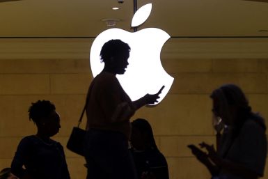 Una mujer usa su dispositivo móvil iPhone mientras pasa frente a un logotipo de Apple iluminado en la tienda de Apple en Nueva York.