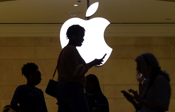 Una mujer usa su dispositivo móvil iPhone mientras pasa frente a un logotipo de Apple iluminado en la tienda de Apple en Nueva York.