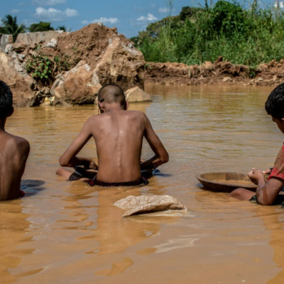 Niños venezolanos trabajan en un charco de agua turbia mientras buscan oro en una mina a cielo abierto