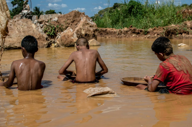 Niños venezolanos trabajan en un charco de agua turbia mientras buscan oro en una mina a cielo abierto