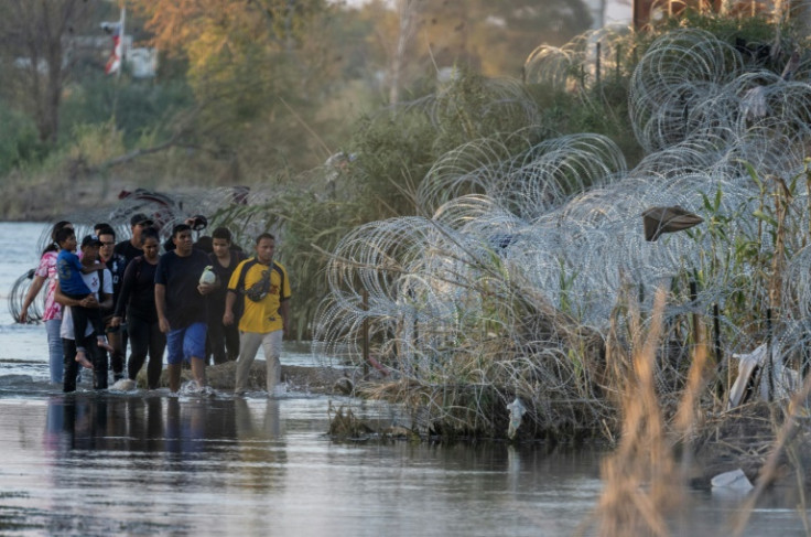 Un grupo de inmigrantes camina a lo largo del Río Grande, cerca de Eagle Pass, Texas, mientras busca un hueco en una cerca de alambre de púas.